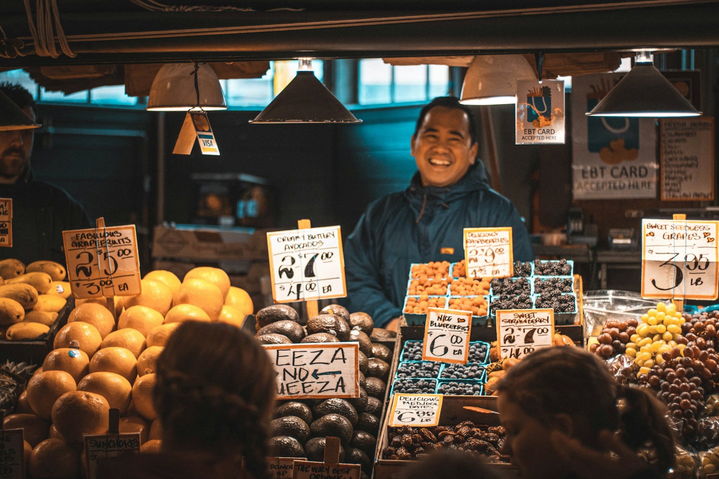 En marknadsförsäljare står bakom ett stånd fyllt med färsk frukt.
